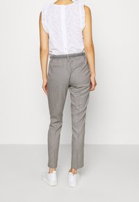 Biała bluzka w stylu eyelet z falbaniastymi rękawami w połączeniu z szarymi spodniami w kratkę o tapered kroju. Spodnie mają elastyczny pas i tylne kieszenie.