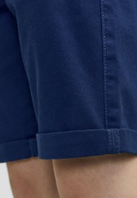 Mørkeblå bomullsshorts med rullesøm, med en glatt tekstur og detaljer i sømmen på siden. Lengde til midten av låret.
