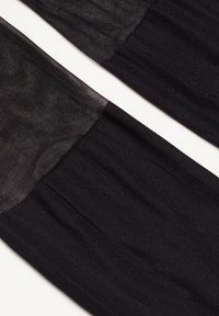 Bas en soie noire avec une partie supérieure semi-transparente, présentant une texture lisse et un éclat subtil, se transformant en une partie inférieure opaque.