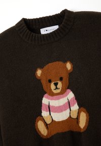 Brauner gestrickter Pullover mit Bärenmotiv und gestreifter rosa und weißer Bluse. Gerippter Rundhalsausschnitt und weiche Textur.