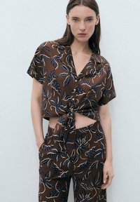 Brown, short-sleeve, button-up top with a tied waist, featuring a leaf pattern in blue and beige. Paired with matching pants.