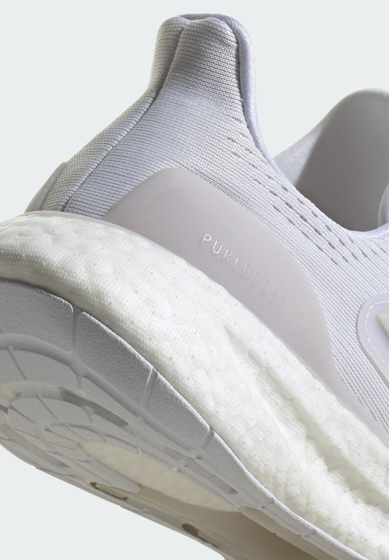 Lichtgrijze hardloopschoen met een bovenwerk van gestructureerde stof, een witte gevoerde middenzool en een gemusterde rubberen buitenzool. Voorzien van "PUREBOOST" lettering.