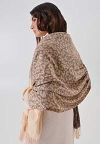 Sciarpa beige a motivo leopardo con bordi frangiati, caratterizzata da una texture morbida e un gradiente che va dal beige chiaro a tonalità più scure.