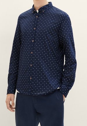 Marineblaues Langarmhemd mit Button-Down-Kragen, versehen mit einem weißen Sternenmuster und braunen Knöpfen. Weiche Textur, taillierte Passform.