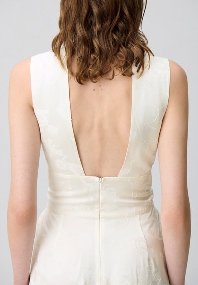 Vestido de marfil con textura floral, espalda pronunciada y cierre de cremallera. Diseño sin mangas con cintura ajustada y tela suave.