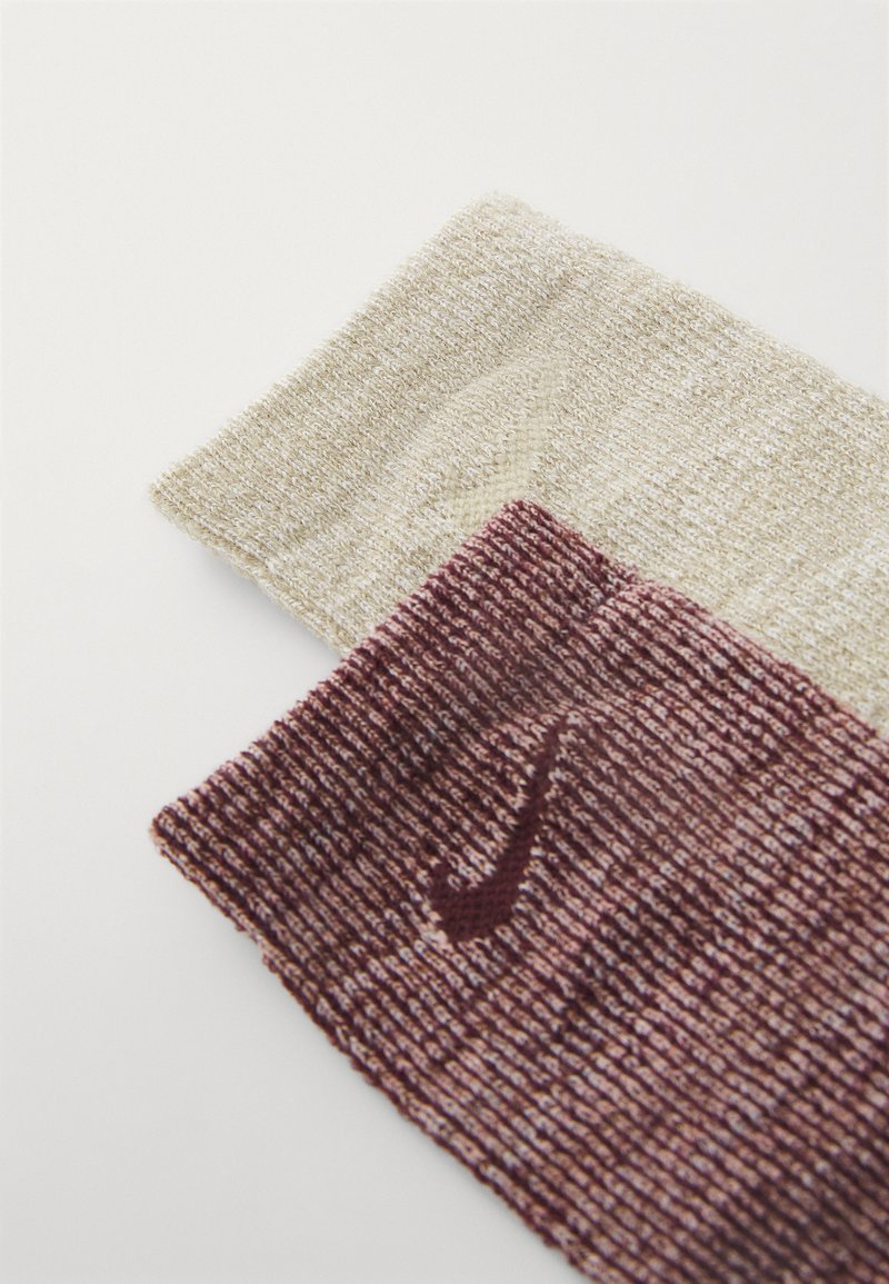 Due copricapi in tessuto lavorato a maglia, uno in beige chiaro e l'altro in bordeaux scuro con un motivo testurizzato e un logo discreto sul band più scuro.