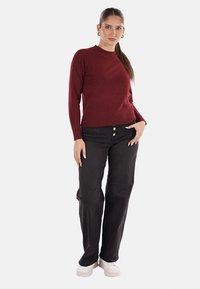 Maglione a maglia bordeaux con maniche lunghe, abbinato a jeans neri a gamba dritta con chiusura a bottoni e sneakers bianche.