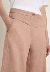 Light pink linen trousers with a button closure, featuring side pockets and a structured waistband. Smooth texture and wide-leg design.