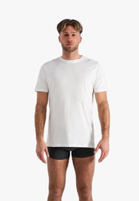 Witte kortekleurige katoenen t-shirt met een ronde hals, gepresenteerd op een mannelijk model. Het shirt heeft een relaxte pasvorm en een zachte textuur.