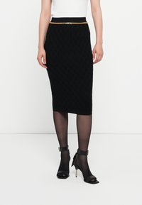Black knee-length pencil skirt with textured pattern, slim fit, and a gold chain accent at the waist. Paired with black ankle strap heels.