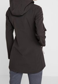 Chaqueta marrón impermeable con capucha, que presenta una silueta ajustada, tejido texturizado y un bolsillo con cremallera en el lateral.