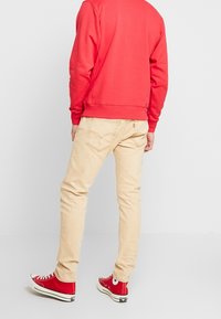 Red sweatshirt, beige jeans, and red sneakers. Notable details include ribbed cuffs and back pocket stitching on jeans. Casual fit.