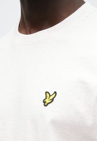 Wit katoenen T-shirt met een klein geel geborduurd vogellogo op de linkerborst. Rondhalsontwerp, gladde textuur, casual stijl.