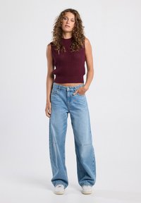 Knit sleeveless top in burgundy with textured pattern; wide-legged light blue denim pants with subtle stitching; white sneakers.