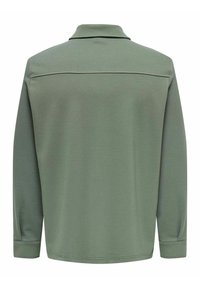 Polo de manga larga en verde apagado, con cuello, textura sutil y dobladillo recto. Sin logotipos ni patrones visibles.