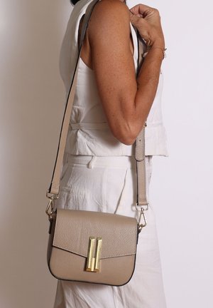 Beige leren crossbody tas met een gestructureerde vorm, accenten van goudkleurig beslag en een klep aan de voorkant. Verstelbare schouderriem voor veelzijdig dragen.