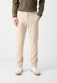 Beige tailored pants made of lightweight fabric with a smooth texture. Features a button closure and side pockets. Worn with white sneakers.