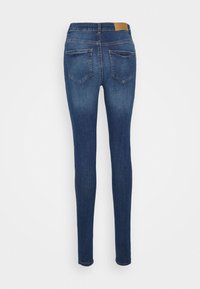 Jeans skinny em denim azul escuro, com uma textura suave, design de cinco bolsos e um patch de couro castanho na cintura.