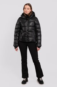 Sort dunjakke med hætte, præget af kviltet design, lynlåslommer og en skinnende overflade. Sammen med sorte bukser og robuste sko.