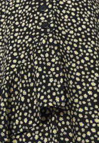 Schwarzer Stoff mit kleinen weißen und gelben Blumenmustern, verziert mit einer Reihe von vier schwarzen Knöpfen und einem plissierten Design.