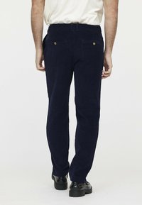 Marineblaue Cordhosen mit geradem Schnitt, ausgestattet mit zwei Gesäßtaschen mit goldenen Knöpfen und gesteppter Detailgestaltung am Bund und an den Nähten.