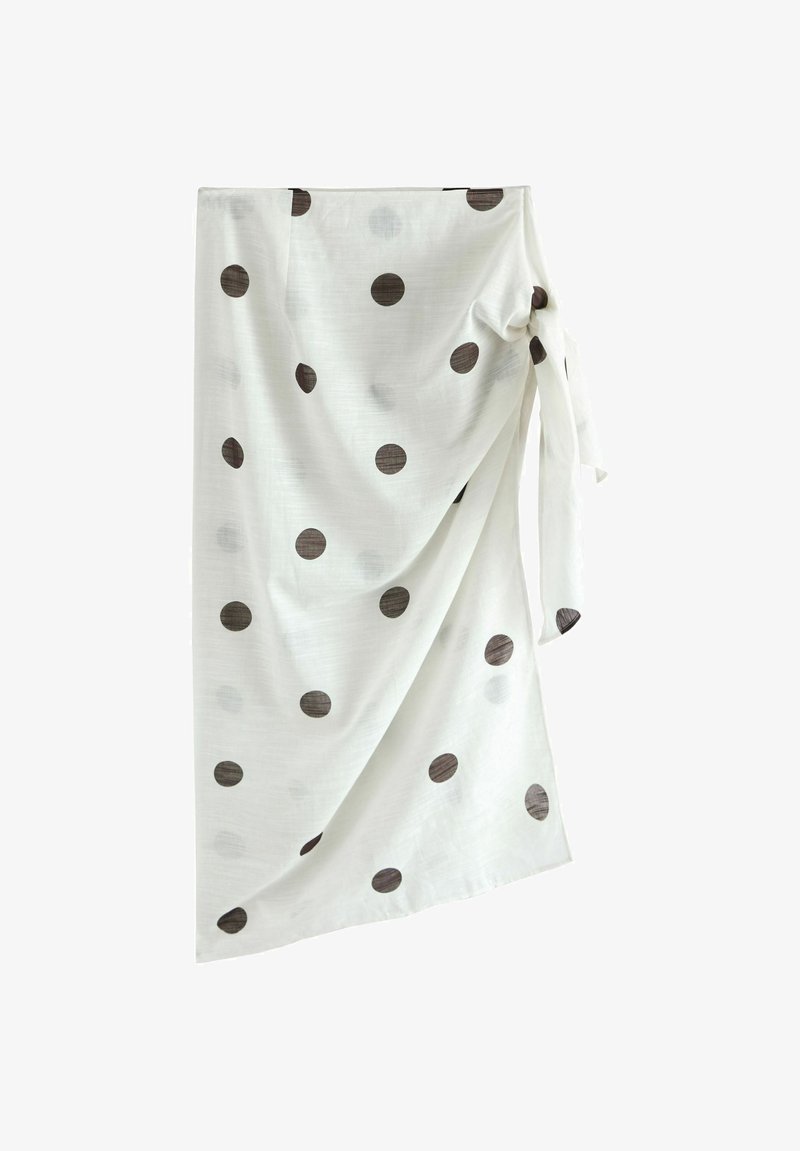 Jupe portefeuille blanche à pois noirs, nouée sur le côté, drapée de plis de tissu doux.