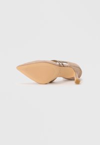 Escarpin beige en daim à bout pointu avec un talon fin et des straps ornés de rhinestones, vu du côté de la semelle.