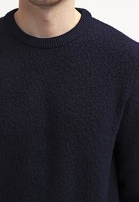 Mörkblå tröja i strukturerad tyg med en mysig känsla; har en ribbad rund halsringning och en något avslappnad passform.