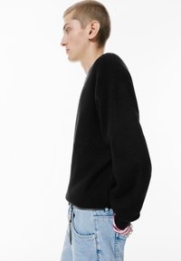 Maglione nero dalla vestibilità ampia e spalle scese, abbinato a jeans chiari a vita alta. Tessuto texturizzato con una superficie liscia.