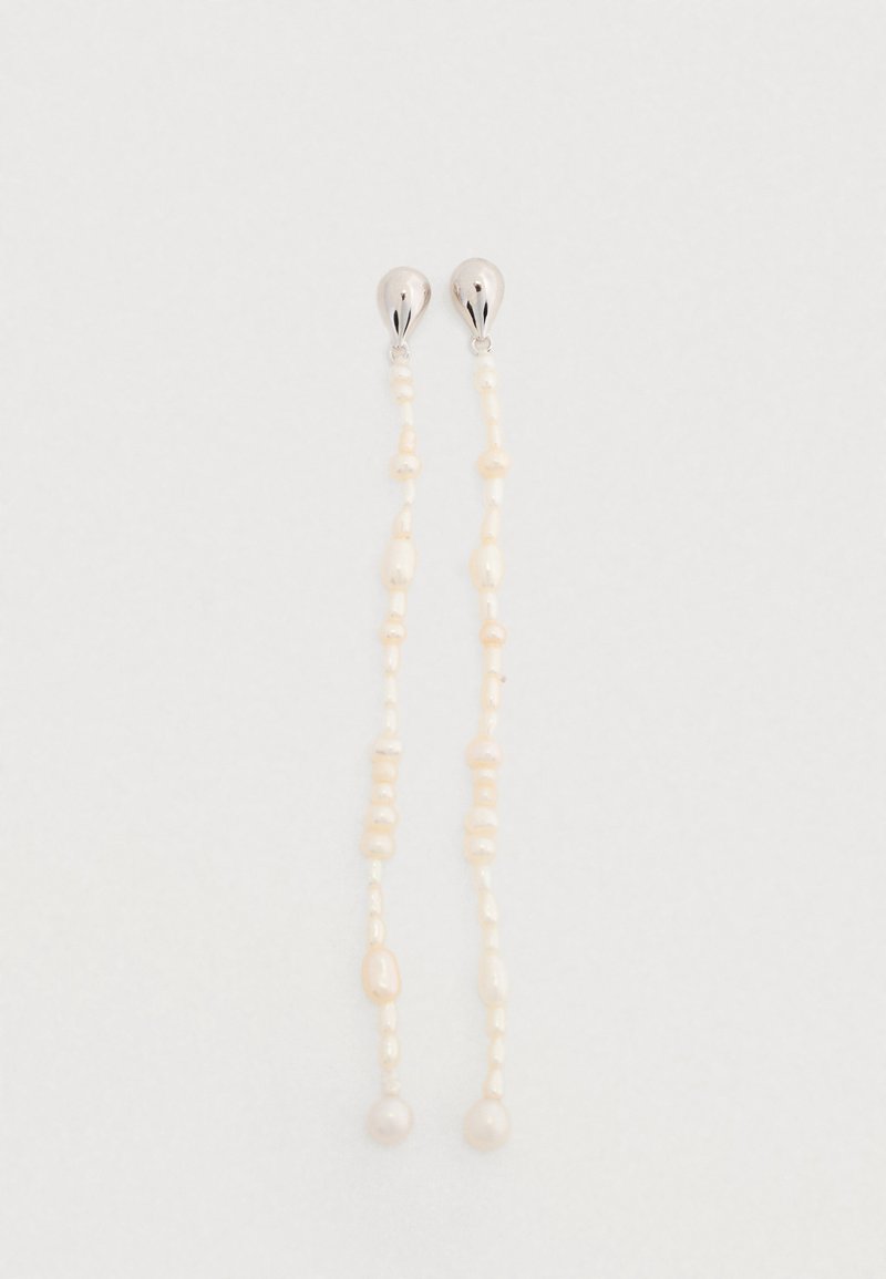 Boucles d'oreilles pendant en perles avec des brins allongés ornés de perles blanches de formes variées et d'accents argentés en haut.