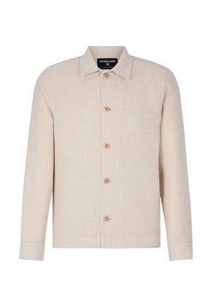 Veste chemise de couleur crème en tissu texturé, avec un devant boutonné, trois boutons visibles et une poche poitrine.