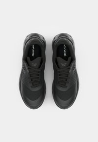Chaussures de sport noires avec une tige texturée, bout rond et lacets plats. Présente des lignes subtiles sur le côté et une semelle rembourrée pour un meilleur soutien.