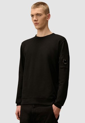Schwarzes, langärmeliges Sweatshirt aus Baumwolle mit Rundhalsausschnitt, gerippten Bündchen und einer aufgesetzten Tasche am linken Arm mit einem runden Akzent.