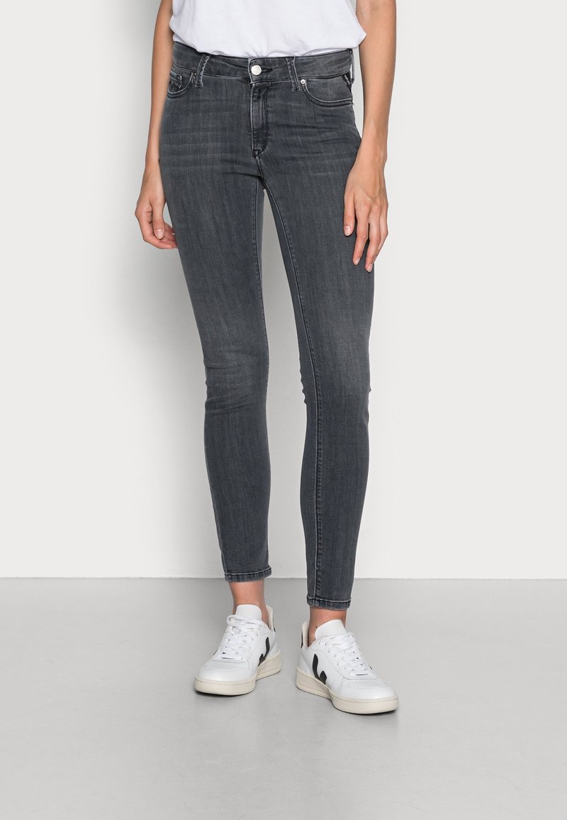 Jeans ajustados de mezclilla en gris oscuro con una cintura alta, que presentan un clásico diseño de cinco bolsillos y un ligero desvanecimiento. Combinados con zapatillas blancas.