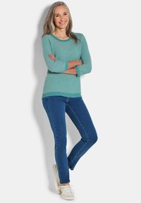 Türkiser gestreifter Pullover mit Dreiviertelärmeln, kombiniert mit körperbetonten blauen Jeans und weißen Sneakers. Der Pullover hat eine gerippte Struktur.