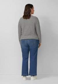 Zwart-witte gestreepte langemouwen top gecombineerd met blauwe flared jeans en witte sneakers, gezien vanaf de achterkant tegen een lichte achtergrond.