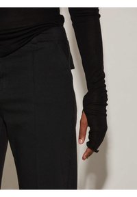 Maglietta nera a manica lunga con design aderente e polsini con foro per il pollice, sopra pantaloni neri con una texture liscia e taglio dritto.