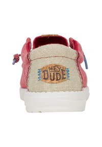 Sneaker rossa in tessuto con un tallone texturizzato beige, caratterizzata da un'etichetta in sughero con la scritta "HEY DUDE" e dettagli di cucitura blu. Ha anche una suola bianca.