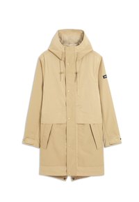 Parka beige à capuche avec fermetures à pression à l'avant, bracelets réglables aux poignets, deux poches avant à rabat et une petite écusson sur la manche gauche.