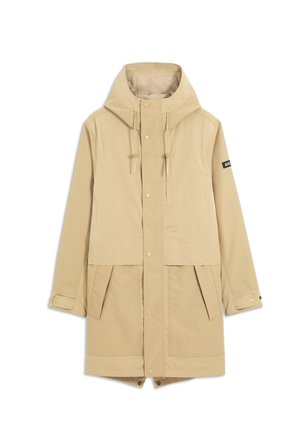 Parka beige à capuche avec fermetures à pression à l'avant, bracelets réglables aux poignets, deux poches avant à rabat et une petite écusson sur la manche gauche.