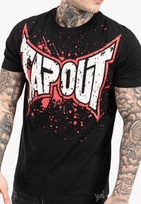 Crna pamučna majica s velikim bijelim i crvenim ''TAPOUT'' grafičkim detaljem, s efektom prskanja. Kratki rukavi i okrugli izrez.