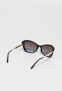 Óculos de sol pretos com armação geométrica, lentes degradê, detalhes em tom dourado nas hastes e pontas das hastes pretas elegantes.