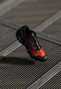 Lengvas juodos ir raudonos spalvos sportinis batelis su violetiniais akcentais, kvėpuojantis viršus, tekstūruotas padas ir greito tvirtinimo sistema. Tinka bėgimui.