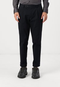 Black pleated trousers with a tailored fit, made of lightweight fabric. Cuffed hems, paired with textured gray sneakers featuring a mesh design.