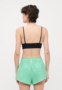 Fekete mintás bralette, állítható pántokkal, párosítva mentazöld rövidnadrággal, rugalmas derékkal és sima textúrával.
