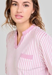 Top de manga larga a rayas en rosa y blanco, con escote en V y un bolsillo en el pecho. Tejido suave con un corte holgado y acentos de canalé.