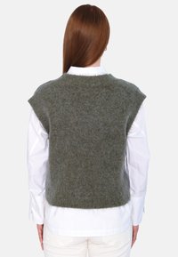 Grønn strikket vest med en myk tekstur, kortermet og rund hals, båret over en hvit skjorte med knapper, vist fra bak.