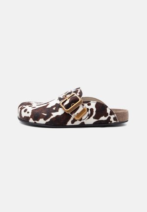Zueco slip-on con estampado de vaca en marrón y blanco, gran hebilla dorada y suela de corcho.