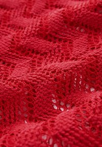 Tessuto di pizzo rosso con intricati motivi floreali e geometrici lavorati a maglia in morbide pieghe.