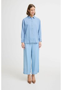 Combinazione di camicia di jeans azzurro chiaro e pantaloni larghi. La camicia con bottoni presenta un colletto; i pantaloni hanno una vestibilità comoda con una texture liscia.